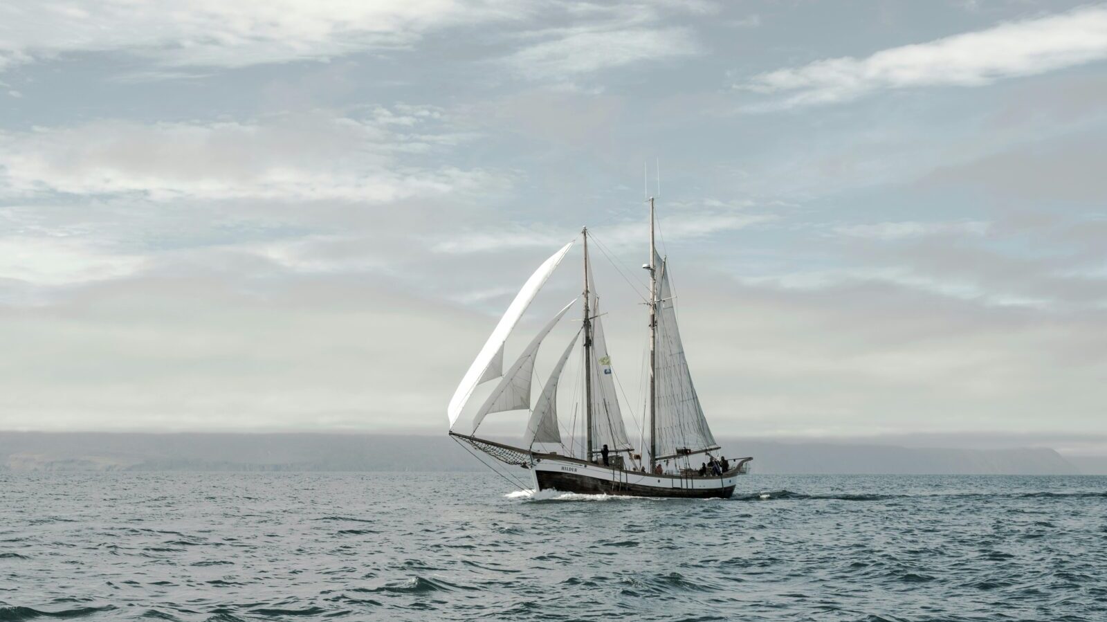 Traditional fishing boat with white hoisted sails floating in middle of wavy sea against beautiful sky